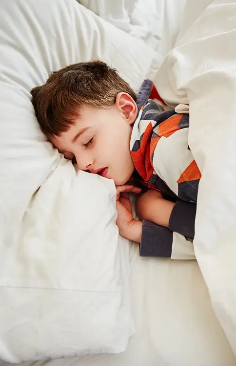 Young child sleeping peacefully in bed wearing colorful pajamas.