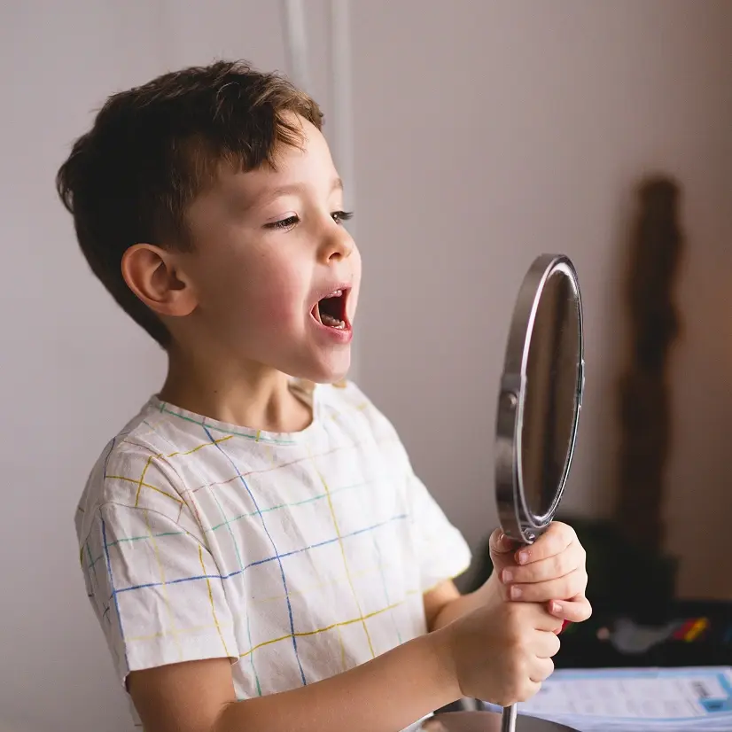 Young boy examining his tongue in a mirror, depicting tongue-tie assessment.