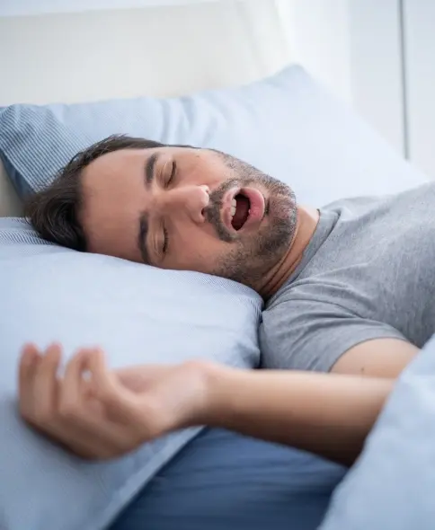 Man sleeping in bed with mouth open, illustrating sleep apnea symptoms.